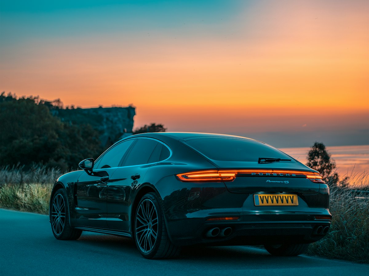 A dark sedan on a coastal road at sunset